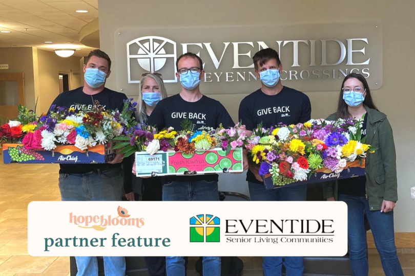 Volunteers standing with flowers in front of an Eventide Sheyenne Crossing sign holding flowers
