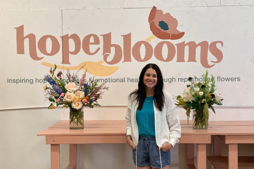woman-standing-in-front-of-flowers-and-hope blooms-sign